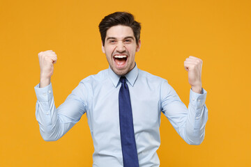 Joyful young business man in classic blue shirt tie posing isolated on yellow wall background...