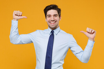 Cheerful young business man in classic blue shirt tie posing isolated on yellow background studio portrait. Achievement career wealth business concept. Mock up copy space. Pointing thumbs on himself.