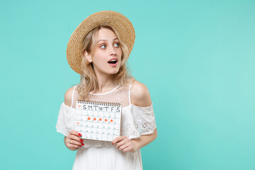 Shocked young woman girl in white dress hat hold female periods calendar for checking menstruation days isolated on blue turquoise background. Medical healthcare gynecological concept. Looking aside.