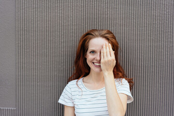 Cheerful woman smiling while covering her left eye
