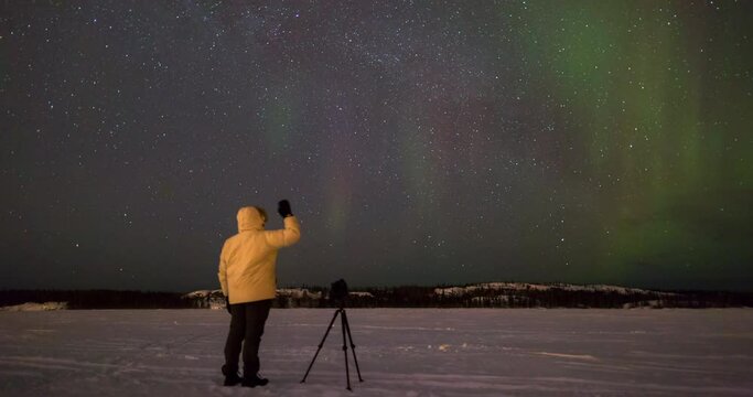 Time lapse shot of tourist photographing and waving at northern lights over snow - Northwest Territories, Canada