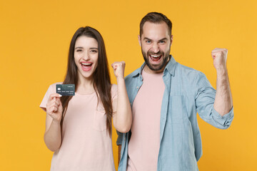 Joyful young couple two friends guy girl in pastel blue casual clothes posing isolated on yellow background. People lifestyle concept. Mock up copy space. Hold credit bank card, doing winner gesture.