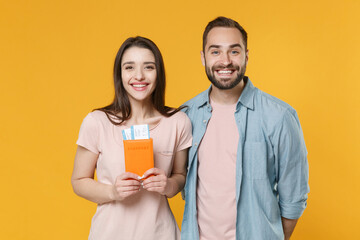 Smiling young couple two friends guy girl in casual clothes isolated on yellow background. Passenger traveling abroad to travel on weekends getaway. Air flight journey concept. Hold passport, tickets.