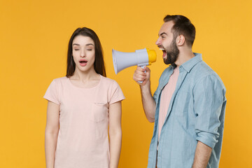 Crazy young couple two friends guy girl in pastel blue casual clothes posing isolated on yellow wall background. People lifestyle concept. Mock up copy space. Scream in megaphone, keeping eyes closed.