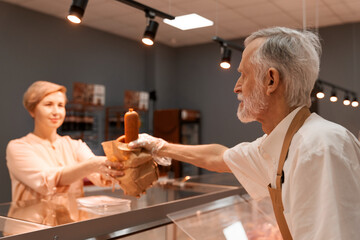 Senior butcher giving sausages to lady.