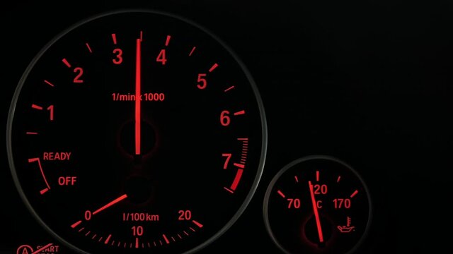 Close up of sports car dashboard with orange luminous dials. PAN to right.