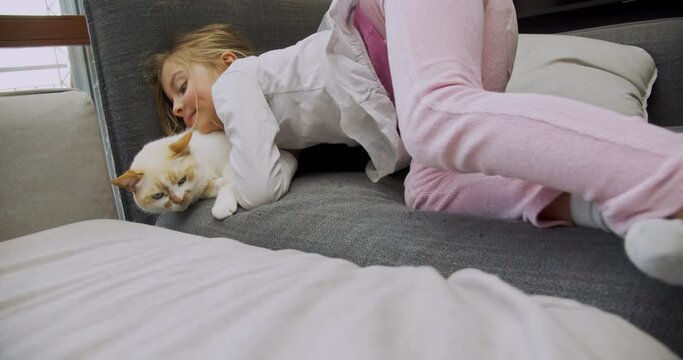 little girl hugging her cats on the couch at home. Kid lying on the sofa while playing with cats.Side view. Child playing with cat at home