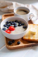Oatmeal with fresh strawberry and blueberry, toast with butter and a cup of espresso coffe for breakfast on wooden tray..