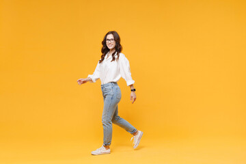 Side view of smiling young brunette business woman in white shirt glasses isolated on yellow background. Achievement career wealth business concept. Mock up copy space. Walking going, looking camera.