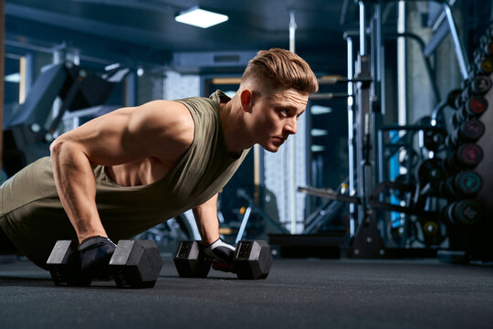Muscular man doing push ups using dumbbells.