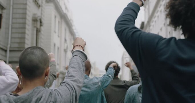 Rear view of a group of activists marching and protesting in the city. Male and female protestors marching on the road giving slogans.
