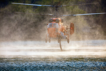 Firefighting helicopter is hovering over the pond to refills water