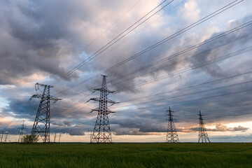 High-voltage power lines passing through a green field of wheat, on the background of a cloudy sky