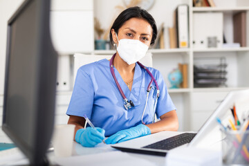 Female doctor in face mask listening to patient complaints at clinic