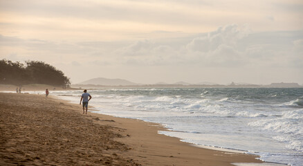 Naklejka premium Man walking along Tannum Sands beach with industry in the background, Gladstone Region, Queensland