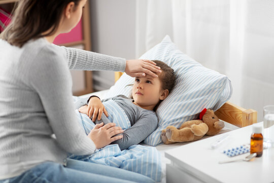 Family, Health And People Concept - Mother Measuring Temperature Of Sick Daughter Lying In Bed At Home With Hand