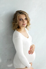Pregnant girl in a white bodysuit. Pregnant woman caressing her belly over gray background. Concepts of pregnancy and family