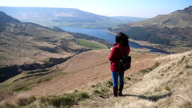 City woman in red jacket enjoying Dove stone reservoir scenery on a sunny day in early spring, handheld camera.