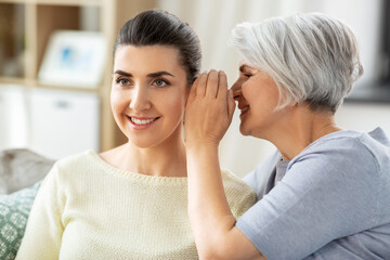 family, generation and people concept - senior mother whispering secret to adult daughter at home