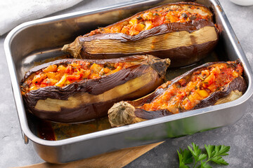 Whole eggplant stuffed with vegetables in baking dish on grey background. Imam bayildi, Turkish cuisine.