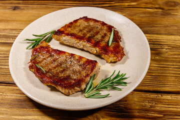 Grilled pork steaks with rosemary on wooden table