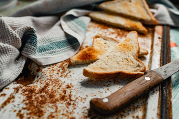 Triangular slices of toasted white bread with a soft texture inside and a crisp crust on the outside on a rusty metal background, next to an old knife with a wooden handle