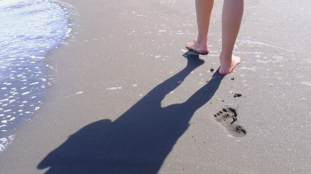 Woman walking alone on ocean sand beach leaving footprint in the dark sand. travel Canary Islands. Slow motion.