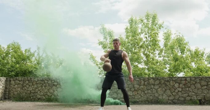 Training with kettlebells, intense strength exercise outdoor with smoke background. Men doing workout with kettlebell