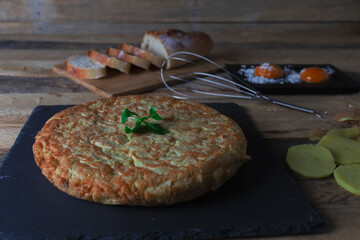 potato omelette with eggs sliced ​​bread sliced ​​potatoes and a whisk, all on a wooden table
