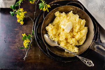 Hot corn porridge with sugar and butter on an old rustic pan and a metal vintage stand. Next to it is a sprig of flowering black currant with yellow flowers