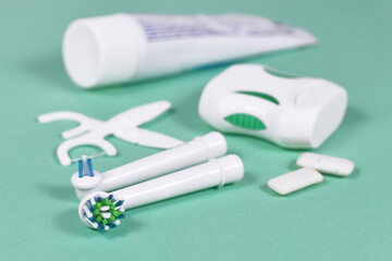 Electric toothbrush heads with other dental care equipment like foss and chewing gum in blurry mint green background