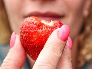 Strawberry berry in a woman's hand on the background of lips, close-up
