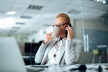 Portrait of a businesswoman drinking tea and talking on smart phone in the office.