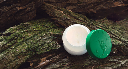 Cosmetic cream jar on tree bark piece side view. Organic cosmetology botanical concept. White...