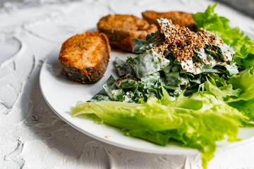 Colorful delicious dish with a salad of sorrel and sour cream, topped with fried sesame seeds, next to fried steaks of red fish pink salmon in breadcrumbs