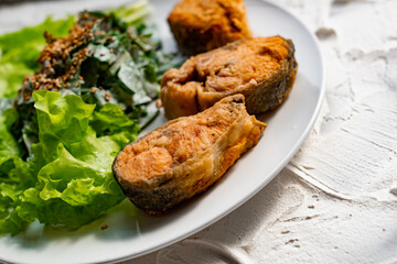 Colorful delicious dish with a salad of sorrel and sour cream, topped with fried sesame seeds, next to fried steaks of red fish pink salmon in breadcrumbs