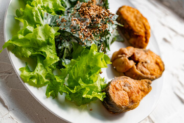 Colorful delicious dish with a salad of sorrel and sour cream, topped with fried sesame seeds, next to fried steaks of red fish pink salmon in breadcrumbs