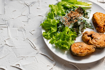 Colorful delicious dish with a salad of sorrel and sour cream, topped with fried sesame seeds, next to fried steaks of red fish pink salmon in breadcrumbs