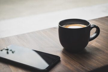Cup of coffee with cellphone on the table in the cafe. Hot latte with mobile telephone in the office. Natural black mug the best start to any morning about business contacts in the restaurant.