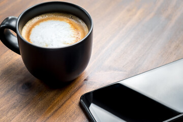 Cup of coffee with cellphone on the table in the cafe. Hot latte with mobile telephone in the office. Natural black mug the best start to any morning about business contacts in the restaurant.