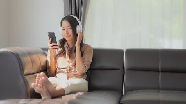 Girl with Headphones on Couch holding Smartphone listening to Music.
