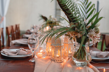 Decorated for wedding elegant dinner table outdoors. Candles, vase woth tropical flowers