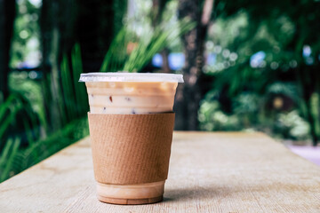 Cold coffee in plastic cup on wooden table at coffee shop. Paper mock up on latte with copy space....