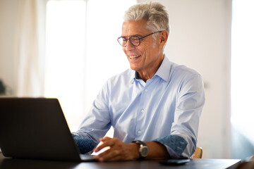 smiling older man sitting at home looking at laptop computer