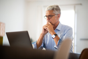 older businessman sitting in office looking at laptop