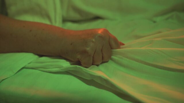Hand of terminally ill patient grabbing bed sheet, death agony in hospital