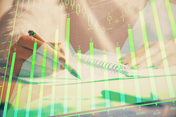 Double exposure of woman's hands making notes with forex graph hologram. Concept stock market...