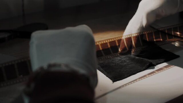 A man working at a film studio examines a film on special analog equipment, film strip goes slowly in hand.Close-up shot.