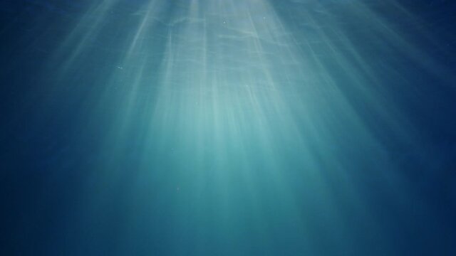 Sunlight beams shining through the deep crystal clear blue-turquoise colored water causing a beautiful lighting reflections curtain with air bubbles rising up to the water surface