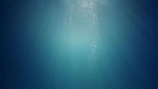 Sunlight beams shining through the deep crystal clear blue-turquoise colored water causing a beautiful lighting reflections curtain with air bubbles rising up to the water surface